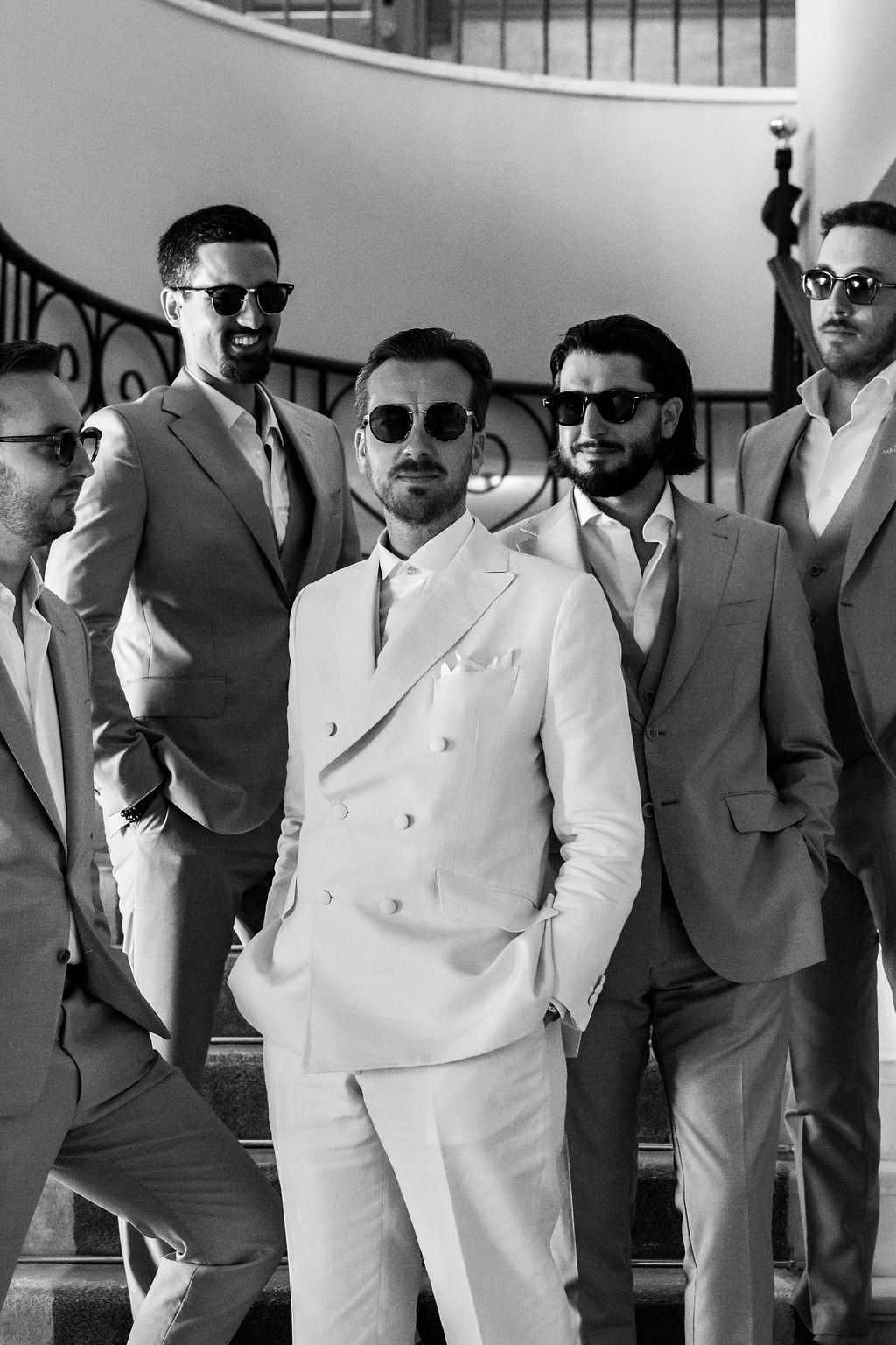 Groom in a white double-breasted suit with his groomsmen by the staircase of a historic estate in Mallorca, photo by Storyteller Photographie – La Promesse, luxury wedding planner in Mallorca